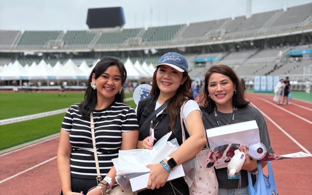 Three friends smiling on the stadium track before a concert in Seoul